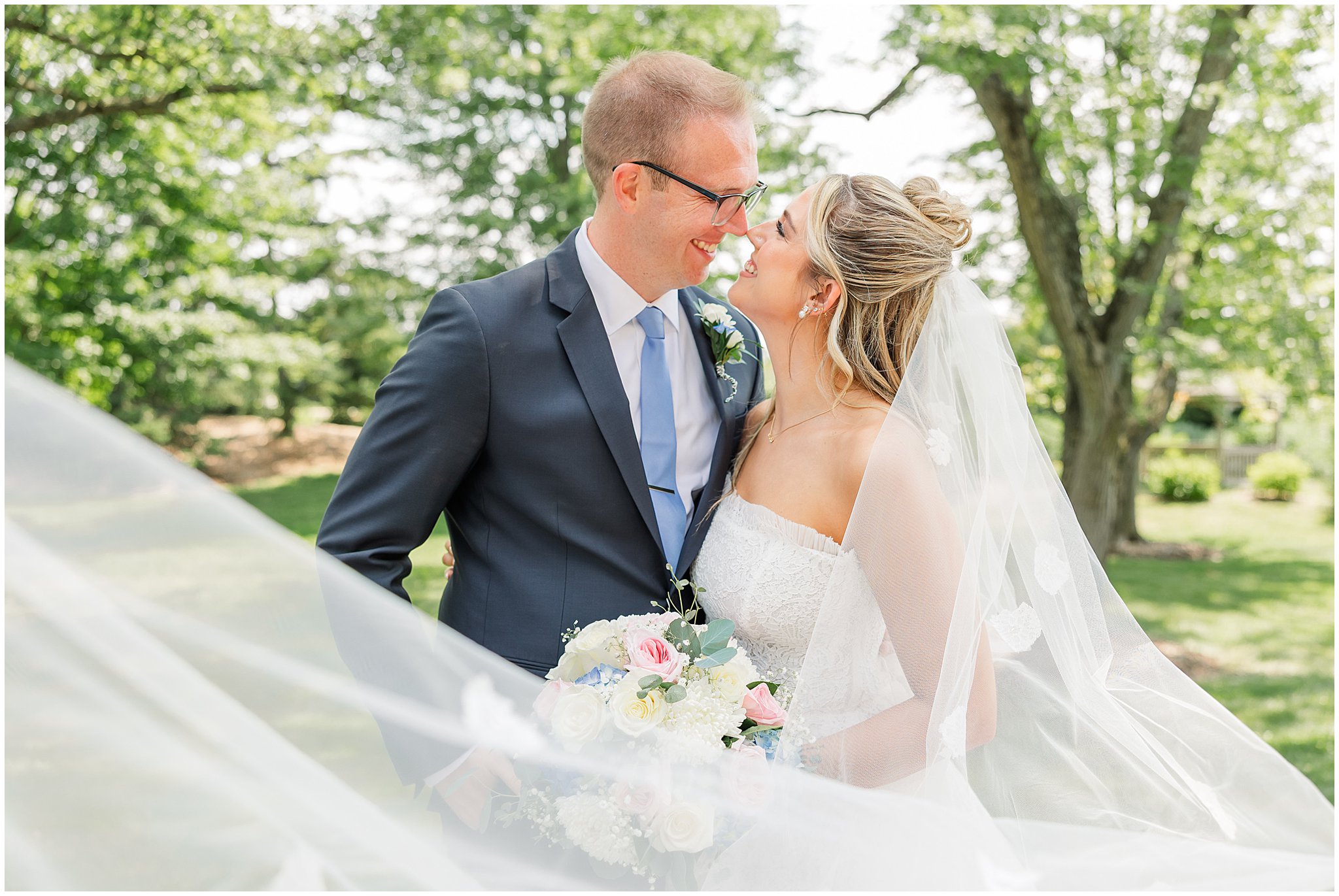 Bride & groom touching noses and smiling at each other, the veil swoops through the composition.